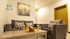 Una sala de estar con dos sofás, una mesa de centro con frutas y bebidas, y un cuadro en la pared.