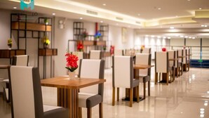 Un comedor moderno con mesas y sillas de madera, un jarrón de flores rojas, y un interior limpio y bien iluminado.