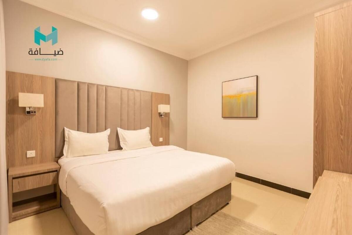 A modern hotel room with a large bed, wooden headboard, bedside lamps, and a framed picture on the wall.