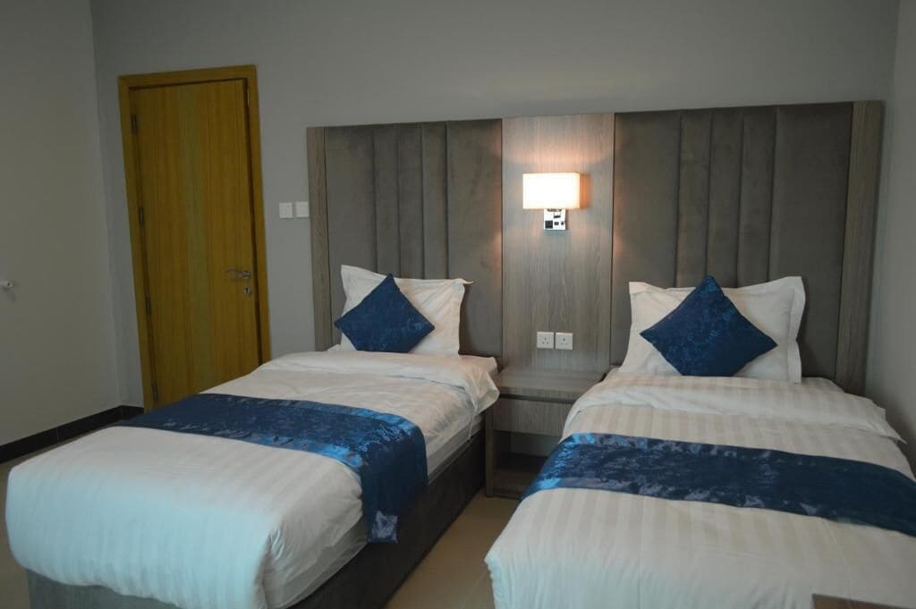 Une chambre d’hôtel avec deux lits, une tête de lit en bois, une table de chevet et une lampe fixée au mur.