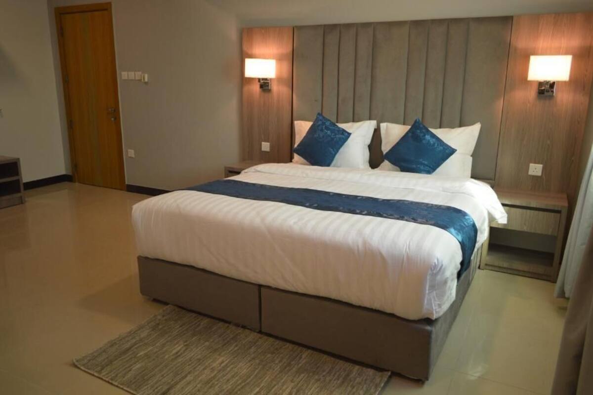 A modern hotel room with a large bed, two bedside lamps, and a wooden headboard.