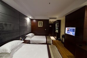 Une chambre d’hôtel avec deux lits simples, un téléviseur fixé au mur et un plancher en bois.