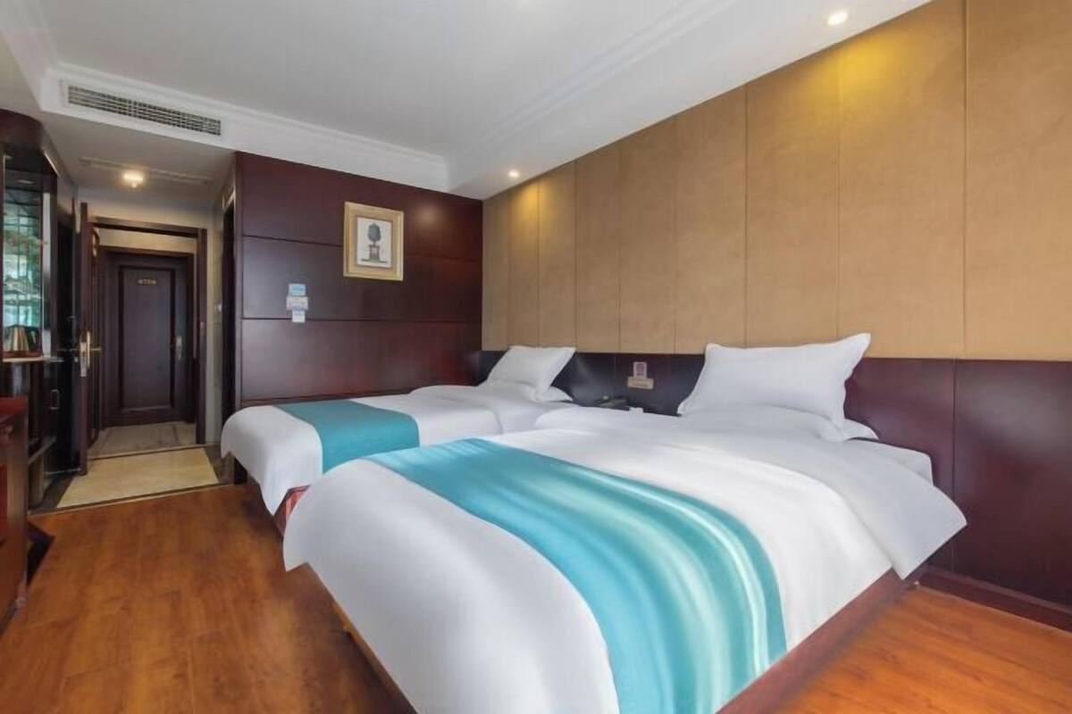 Een hotelkamer met twee bedden, houten vloeren, een donker hoofdeinde en een ingelijst schilderij aan de muur.