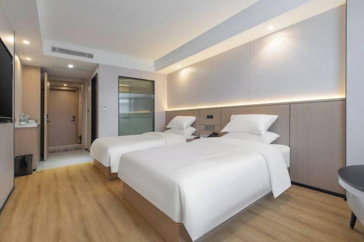 Een hotelkamer met twee bedden, een klein bureau, een spiegel en een zichtbare badkamer door een geopende deur.