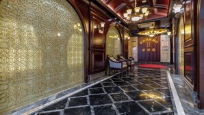 Un hall d’hôtel luxueux, avec un sol en marbre, des panneaux muraux richement décorés et des meubles classiques.