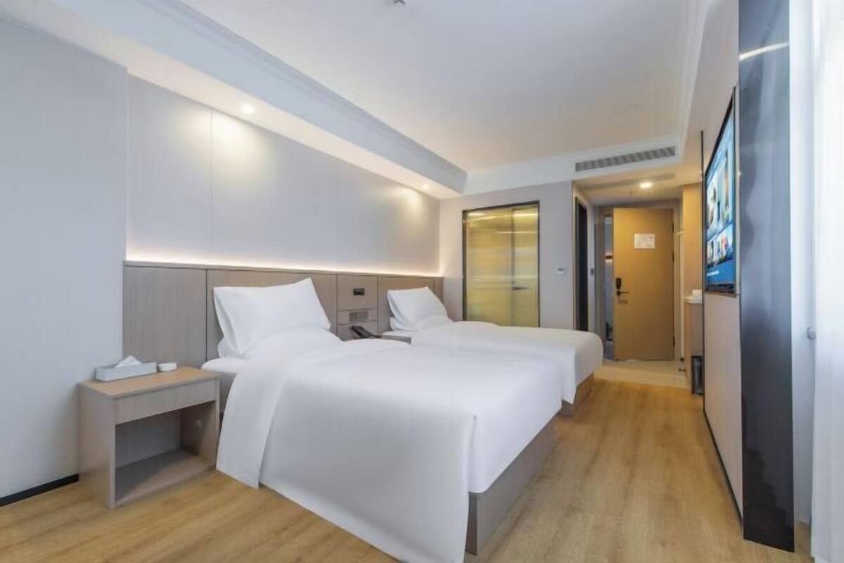 Een hotelkamer met twee bedden, een nachtkastje, een televisie en een deur naar een badkamer.