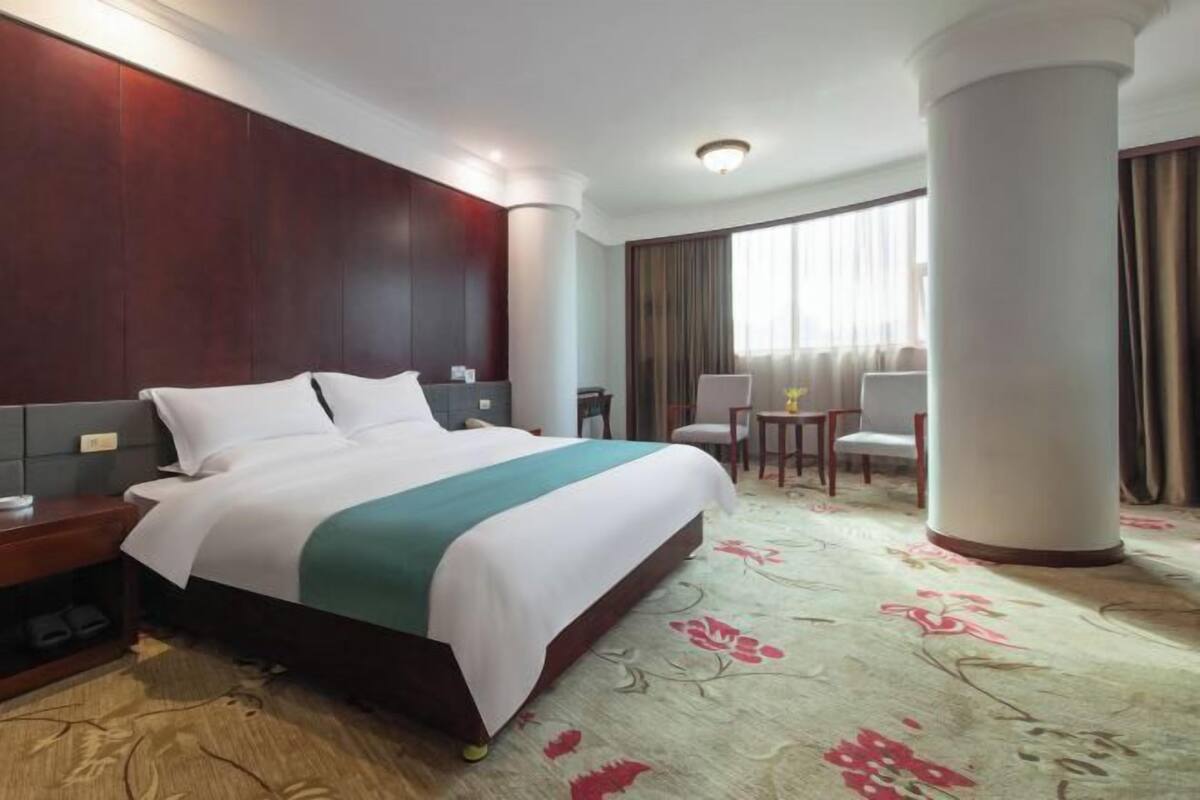 Een hotelkamer met een groot bed, een bureau, een stoel en een raam met gordijnen.