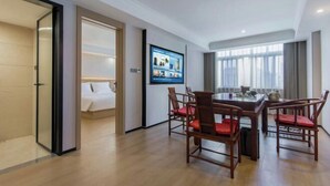 Une chambre d’hôtel avec un lit, un téléviseur fixé au mur, une table à manger avec des chaises et une grande fenêtre.