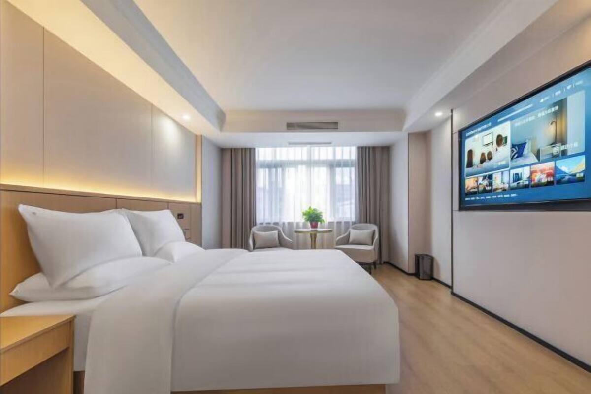 Een hotelkamer met een groot bed, een televisie aan de muur, een klein tafeltje en twee stoelen.