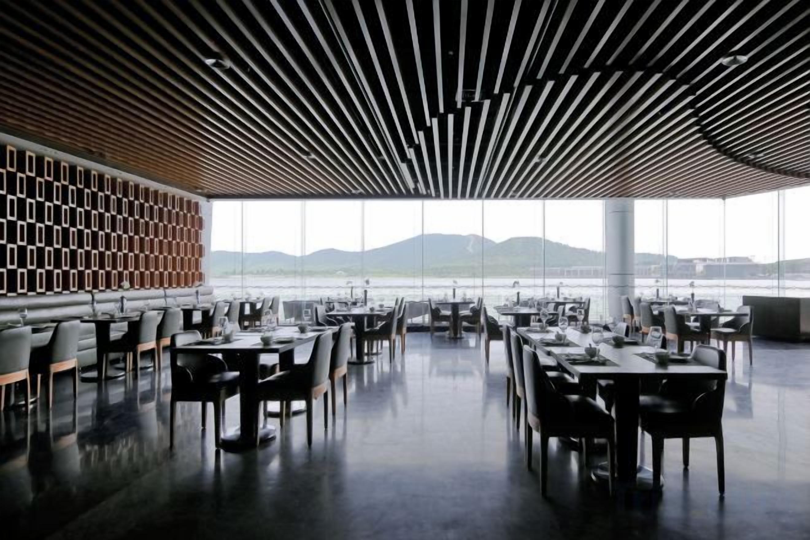 An indoor dining area with tables and chairs, large windows, and a view of the outdoors.