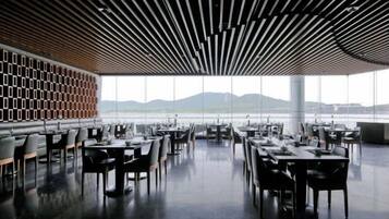 An indoor dining area with tables and chairs, large windows, and a view of the outdoors.