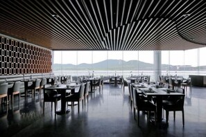 Un comedor interior con mesas y sillas, ventanas grandes y vistas al exterior.