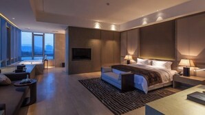 Quarto de hotel moderno com uma cama grande, televisão de tela plana, sofá e vista para a cidade.