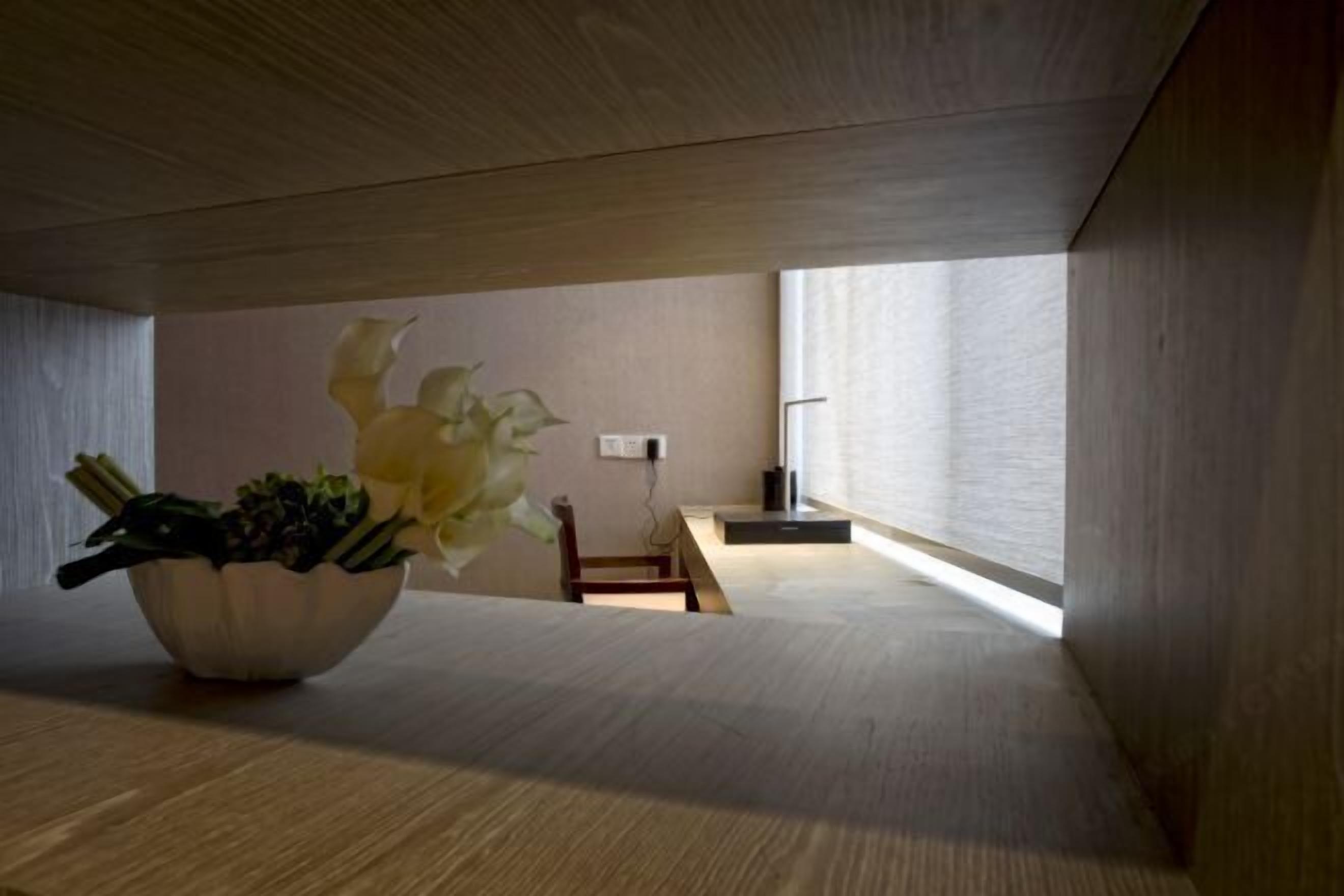 A minimalist room with a wooden floor, a large window, and a bowl of flowers on a table.