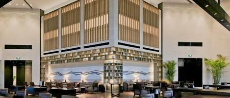 A modern lobby with a central seating area, a large vertical structure with patterned panels, and a wall-mounted artwork.