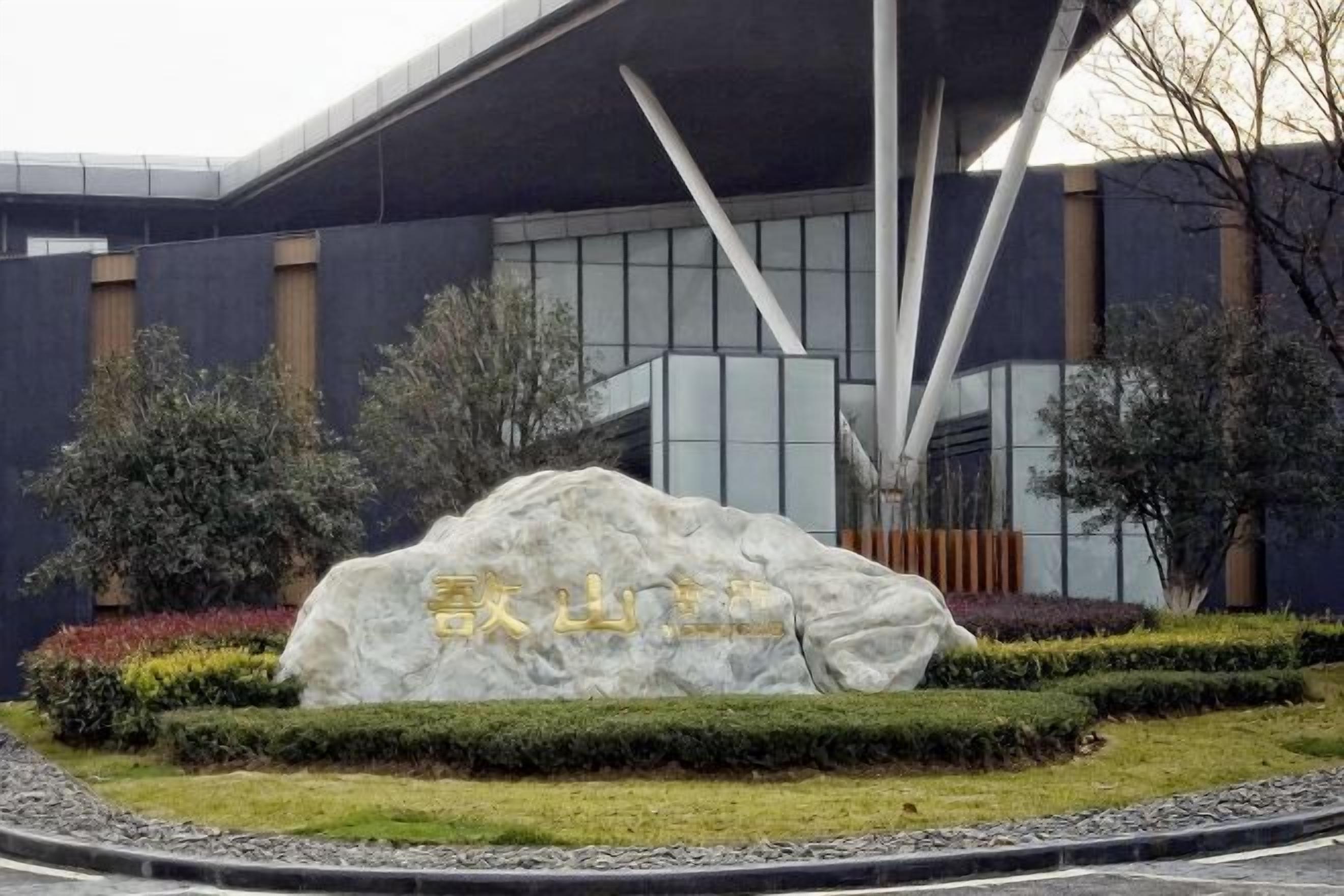 Un bâtiment moderne doté d’une architecture originale, avec un grand rocher orné d’inscriptions en son avant-plan.