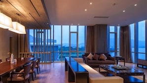 Quarto de hotel moderno com área de jantar, sofá e janelas amplas com vista para a cidade.
