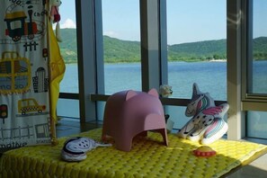 A room with a large window overlooking a lake, a pink stool, and plush toys on a yellow mat. - Arcadia Hotel (Jiangyin)