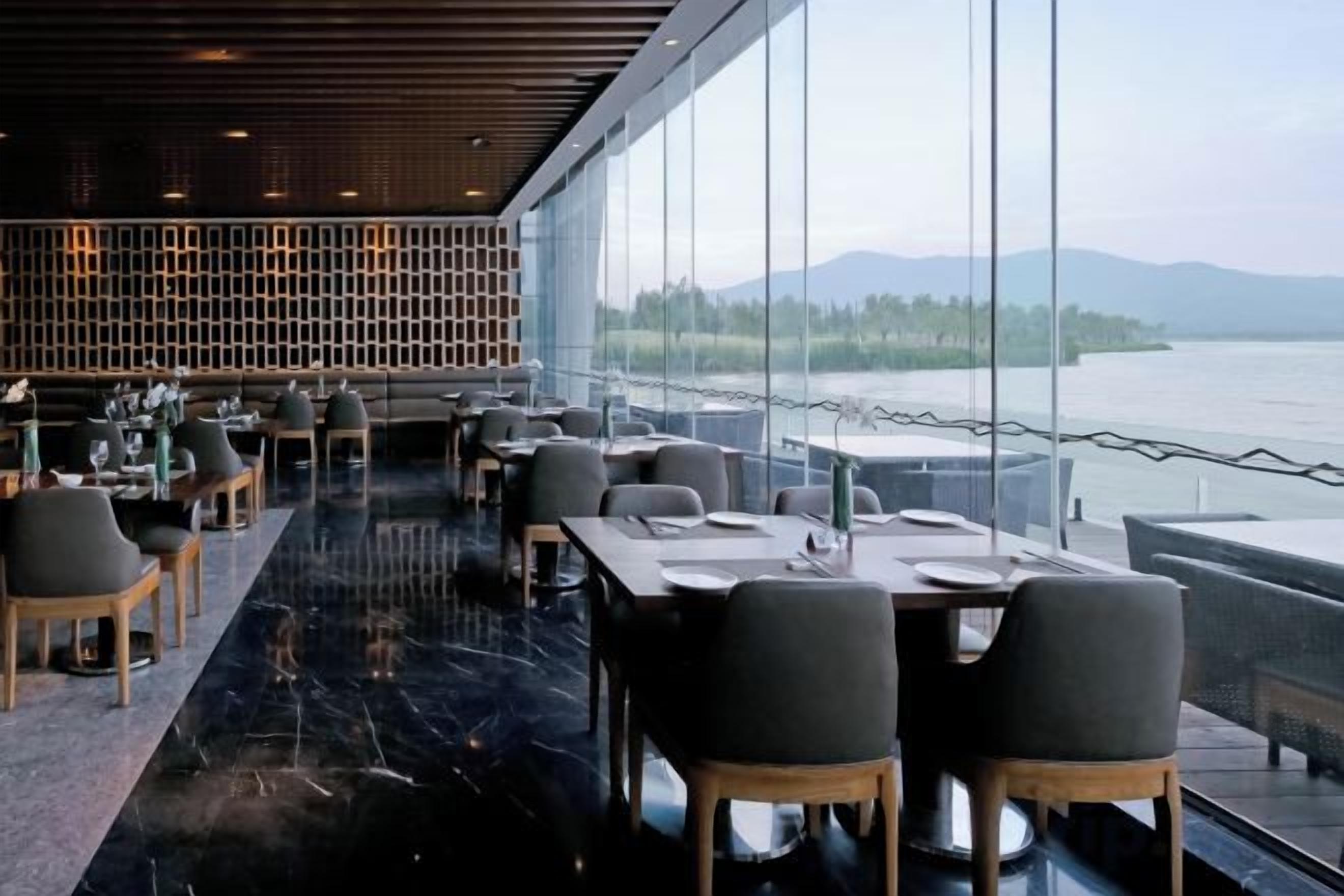 Un restaurante con vistas a un lago, mesas y sillas dispuestas para comer, y una decoración de estilo moderno.