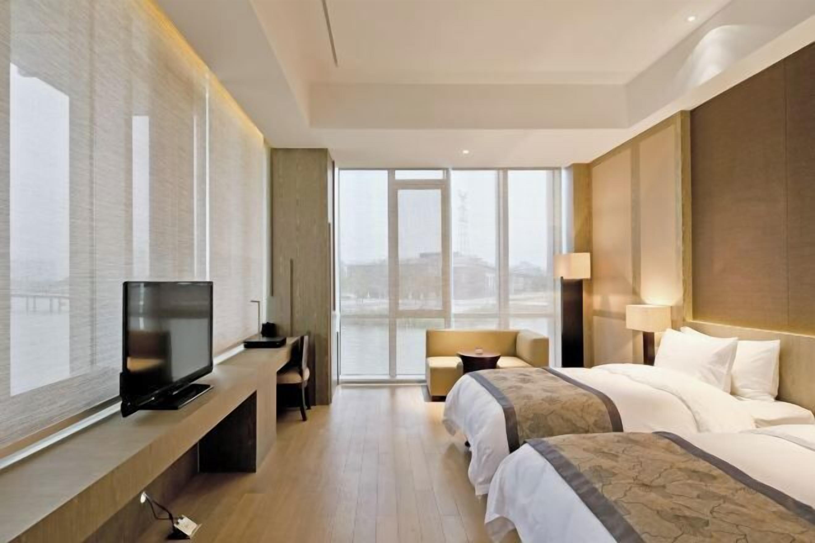 Una habitación de hotel moderna con un ventanal grande, un televisor de pantalla plana, un sofá, una cama y un escritorio.