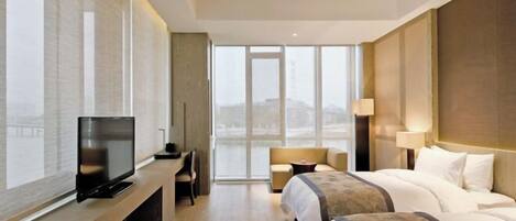 Een moderne hotelkamer met een groot raam, een flatscreen-televisie, een bank, een bed en een bureau.