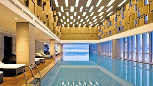 Piscina com padrão geométrico no chão, terraço com espreguiçadeiras e vista para o mar por grandes janelas.