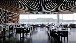 Uma sala de jantar moderna com mesas e cadeiras, janelas amplas e vista para as montanhas.