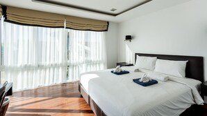 Habitació d'hotel amb un llit gran, un escriptori i una finestra amb cortines translúcides.
