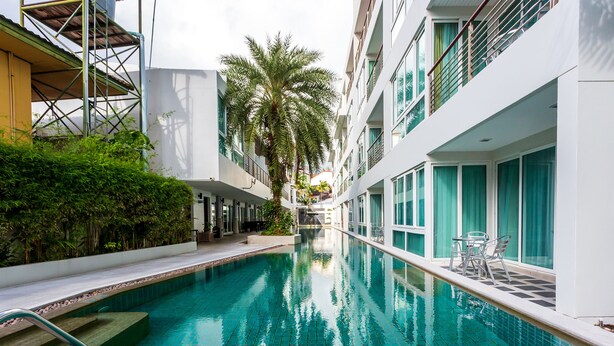 Una piscina amb solàrium d'rajola, envoltada de verdura i edificis moderns.