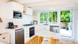 A modern kitchen with white cabinetry, a built-in microwave, a coffee machine, and a sink. - Pointbreak Studio (Te Awanga)