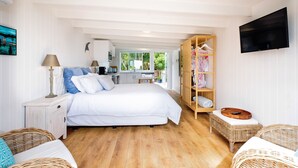 A bedroom with a bed, bedside tables, a TV, a wardrobe, and a view of the outside. - Pointbreak Studio (Te Awanga)