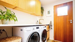 A laundry area with a washing machine, a wooden cabinet, a potted plant, a towel rack, and a door. - Pointbreak Studio (Te Awanga)