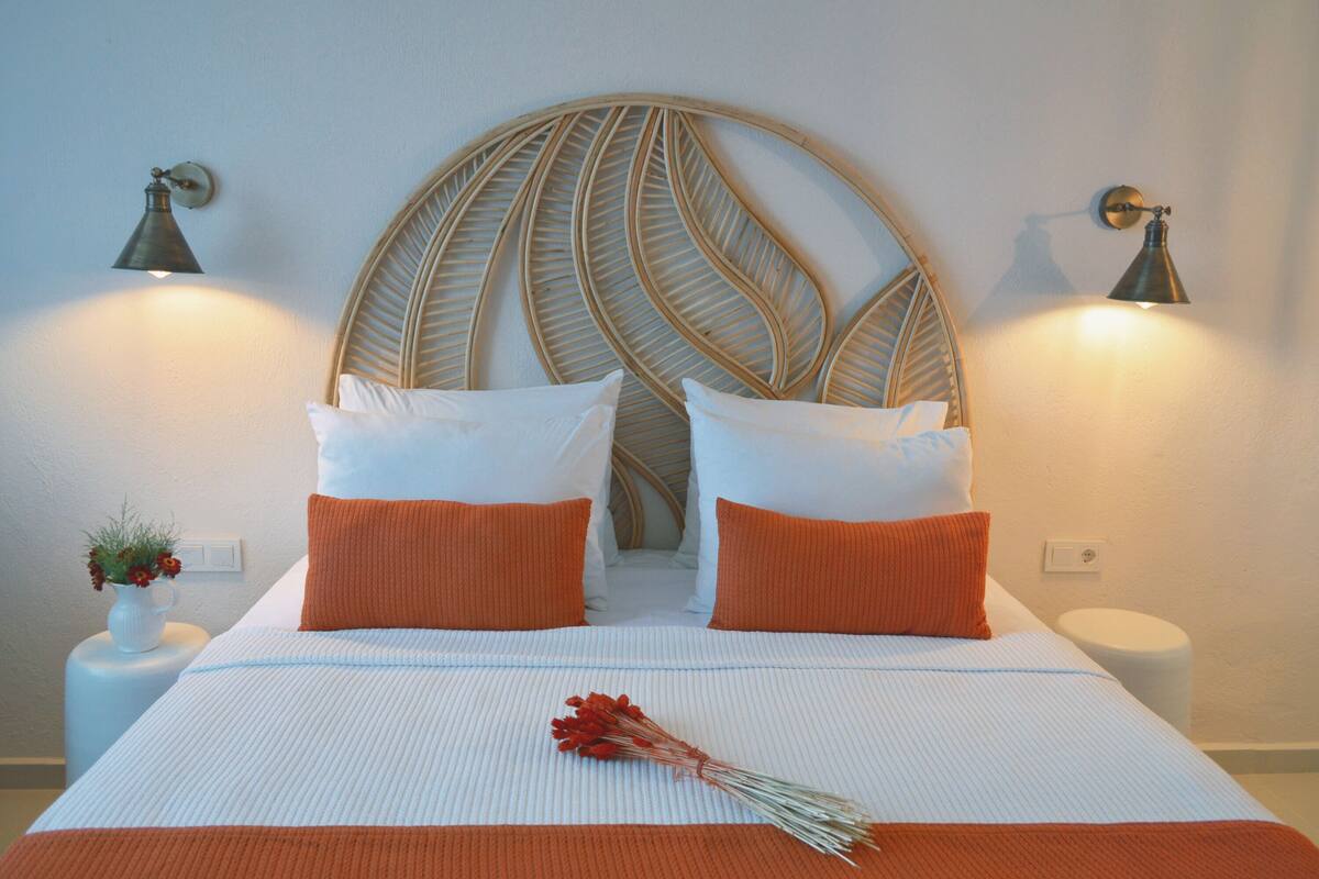 A neatly made bed with white and orange bedding, a decorative headboard, and two wall-mounted lamps.