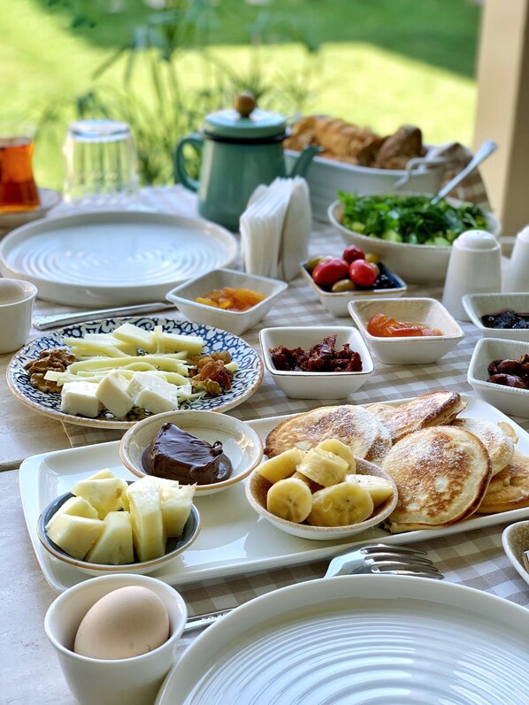 A breakfast table with various dishes including pancakes, fruits, and condiments.