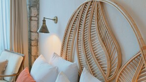 Una cama con almohadas blancas y anaranjadas, un cabecero de mimbre y una lámpara en la pared.
