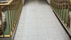 A corridor with tiled flooring, benches, and a stone wall backdrop. - Hotel Paris (San Juan de los Lagos)
