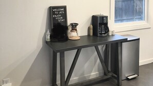 Una cocina con cafetera, un letrero y estantes con tazas y un florero.