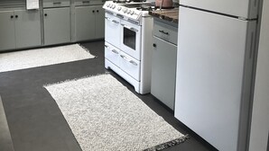 Una cocina moderna con armarios blancos, una estufa, un refrigerador y dos alfombras en el suelo.