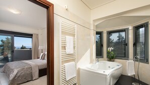 Ein modernes Badezimmer mit Badewanne, einer Duschkabine aus Glas und einem großen Fenster mit Jalousien.