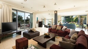Ein geräumiges Wohnzimmer mit großem Flachbildfernseher, bequemen Sitzgelegenheiten und Blick ins Freie.