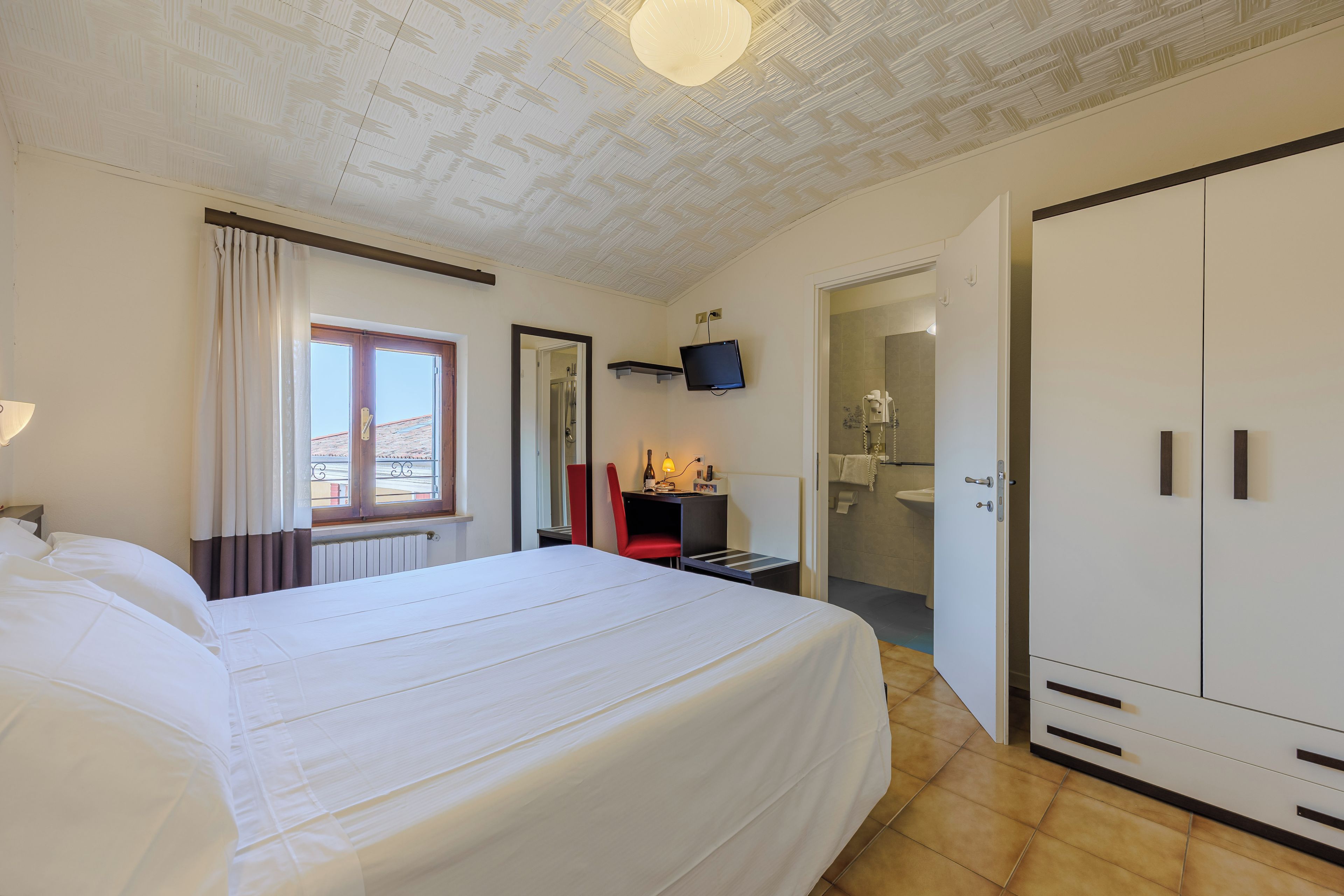 A hotel room with a large bed, a desk with a chair, a television, and a wardrobe.