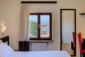 A hotel room with a bed, a window with curtains, a radiator, a door, and a chair. - Hotel Alla Torre (Garda)