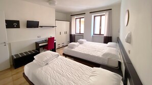 Habitación de hotel con dos camas, un escritorio, una silla, un televisor y una ventana con cortinas.