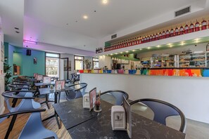 Un interior de restaurante con mesas, sillas, una zona de bar con botellas y vistas por la ventana.