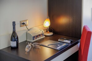 Escritorio de hotel con una botella, vasos, una lámpara, un control remoto y una libreta.