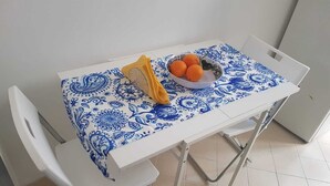 A dining table with a blue and white patterned tablecloth, a bowl of oranges, and a yellow package on it.