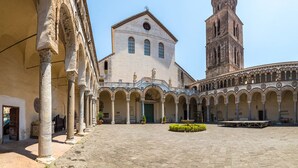 A courtyard with a central building featuring a bell tower, surrounded by arches and columns.