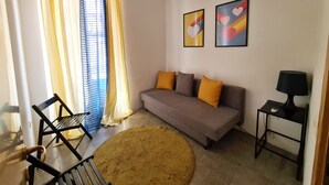 A living room with a sofa, two cushions, a round rug, a chair, a table with a lamp, and two framed pictures on the wall.