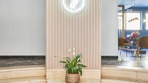A modern interior with a central staircase, a vertical wooden panel with lights, and a potted plant. - Hotel Astoria (Garda)
