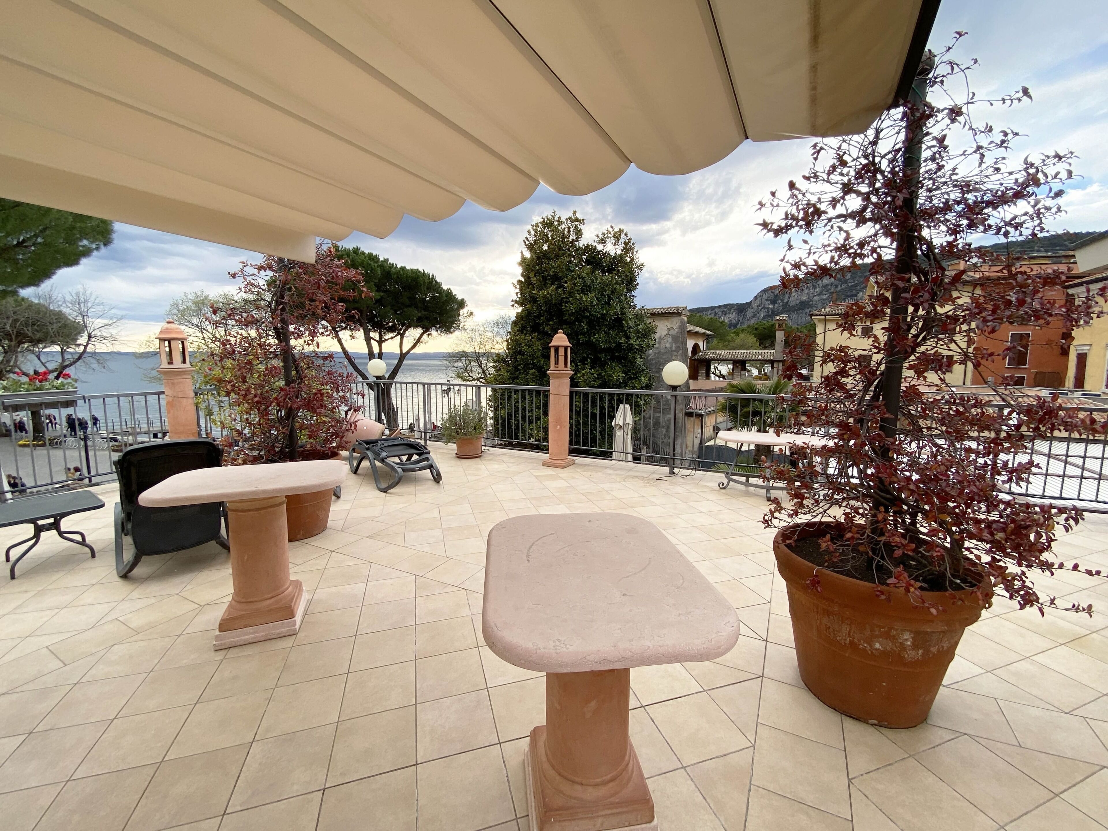 Una terrazza esterna con pavimento piastrellato, un tavolo, sedie e piante in vaso.